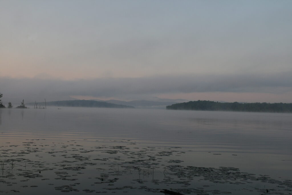 Morning light rising over Lake Umbagog with soft color on calm water in the Umbagog National Wildlife Refuge.