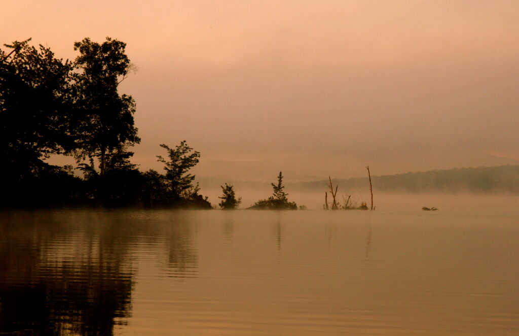 Soft golden light filtering through morning fog over the still waters of Lake Umbagog, peaceful New England nature photography.