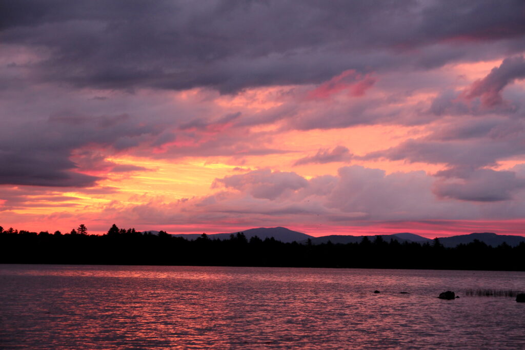 Warm, glowing sunset colors reflecting across the quiet waters of Lake Umbagog in a remote wilderness setting.