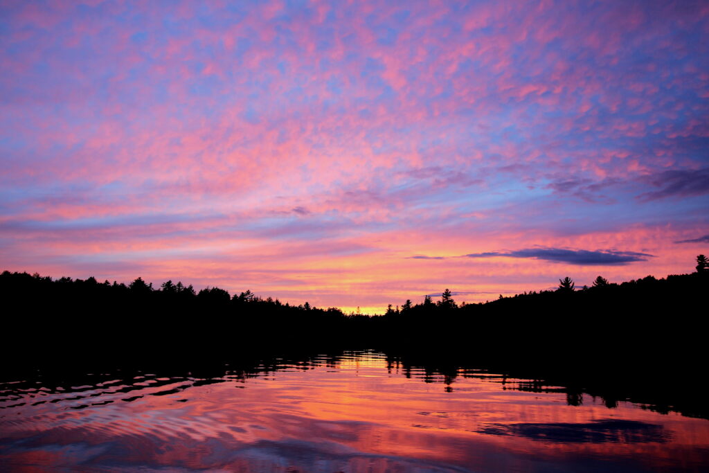 Purple dusk light over calm Lake Umbagog with soft lavender reflections, peaceful nature photography.