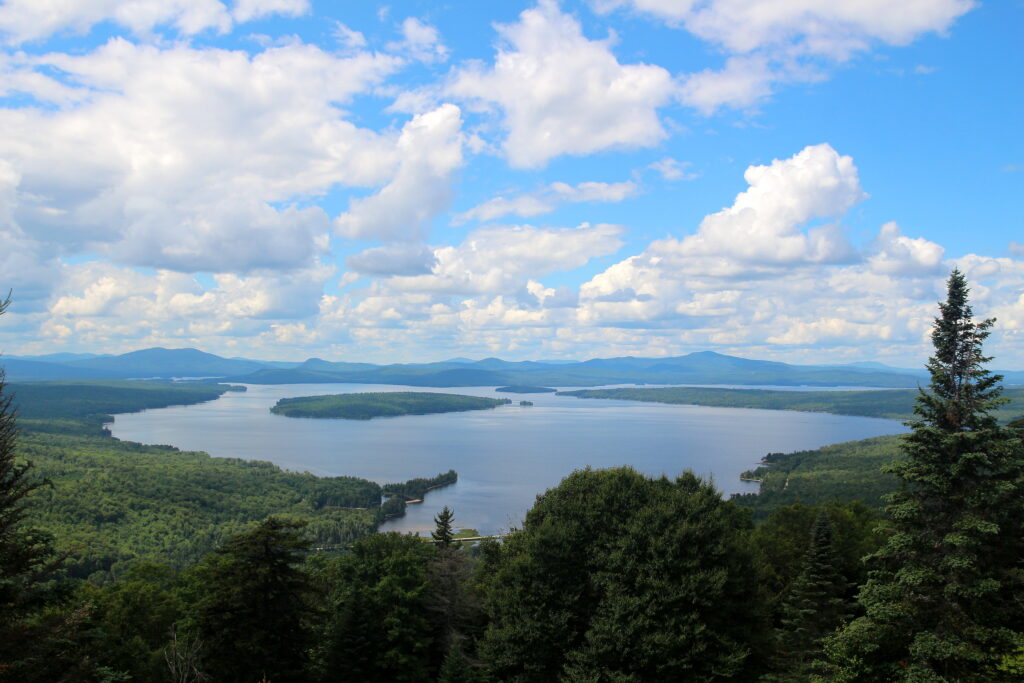 Blue sky and drifting clouds reflected on the clear waters of Lake Rangeley in East Rangeley, creating a peaceful healing‑in‑nature scene.