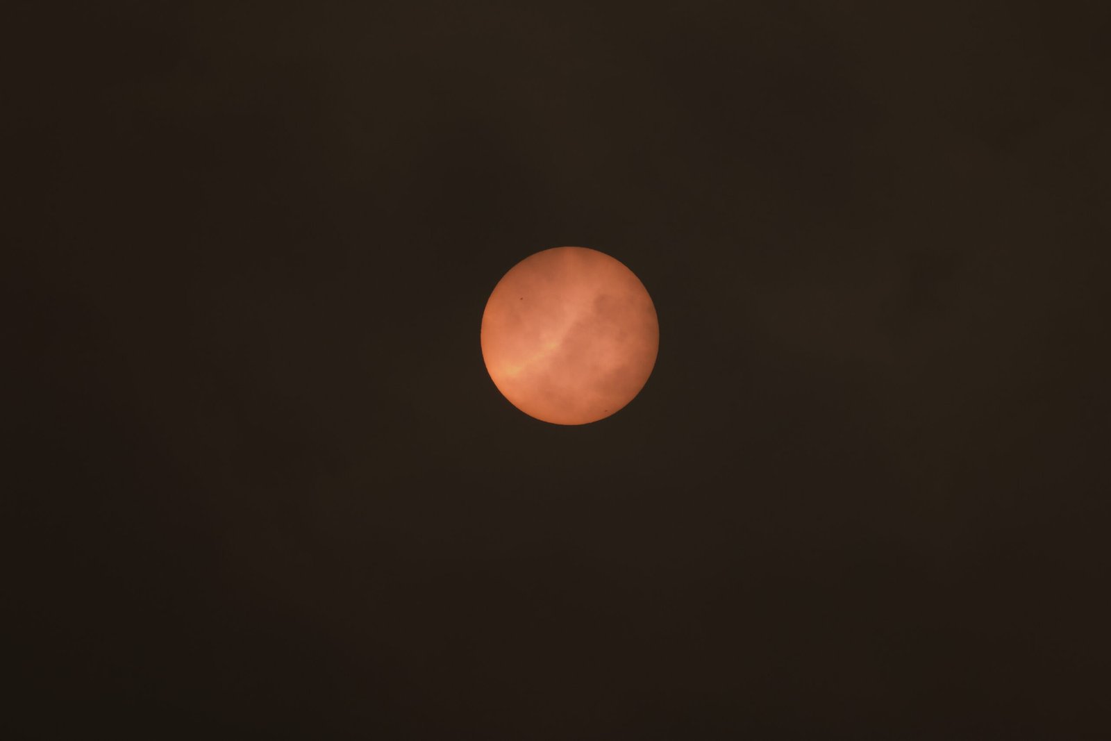 Fiery solar disc showing sunspots filtered through wildfire smoke in Pomfret, Connecticut