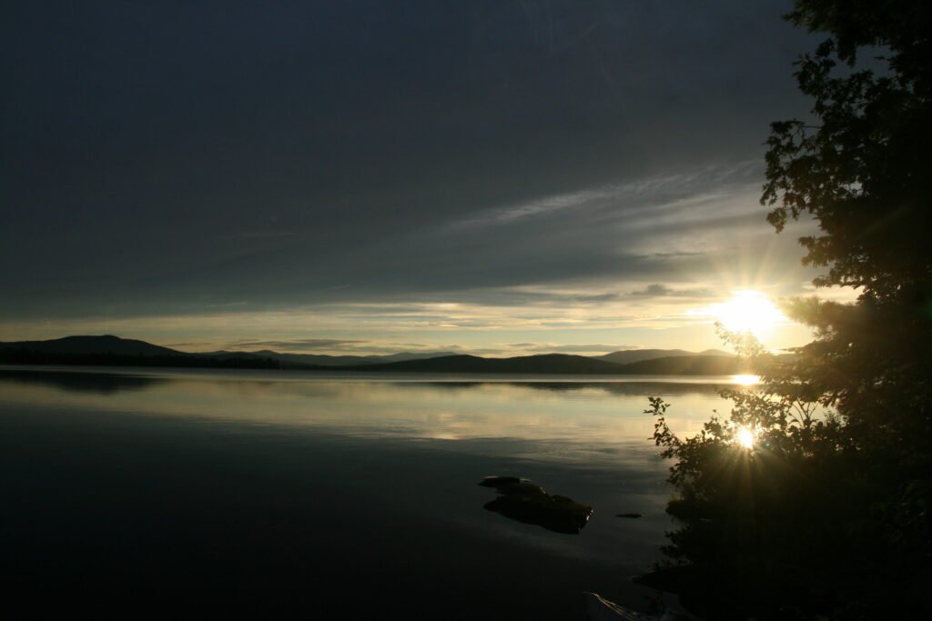 Golden sunset reflecting over the calm waters and silhouetted trees of Lake Umbagog