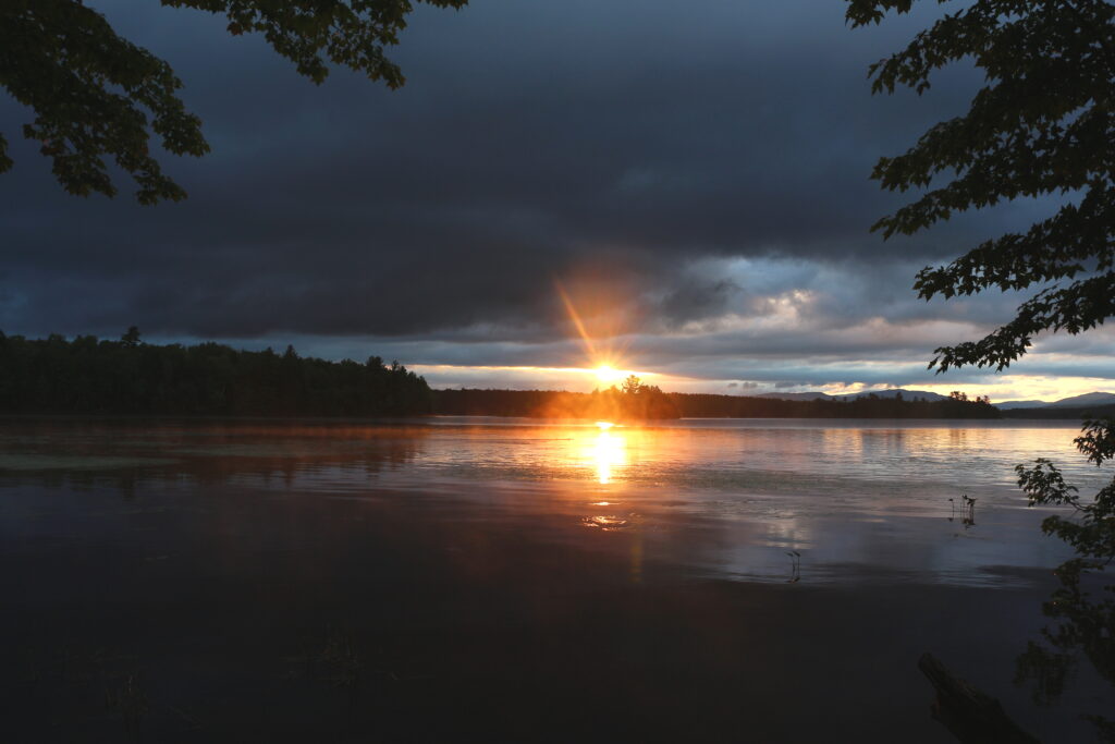 Vibrant sunrise breaking through clouds over the water and distant shoreline of Lake Umbagog, New Hampshire