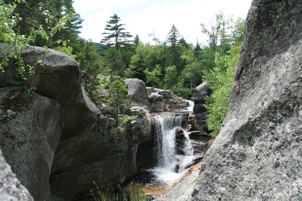 Wide view of Screw Auger Falls showing carved rock gorges, evergreens, and grasses above the rocks at Grafton Notch State Park, Maine