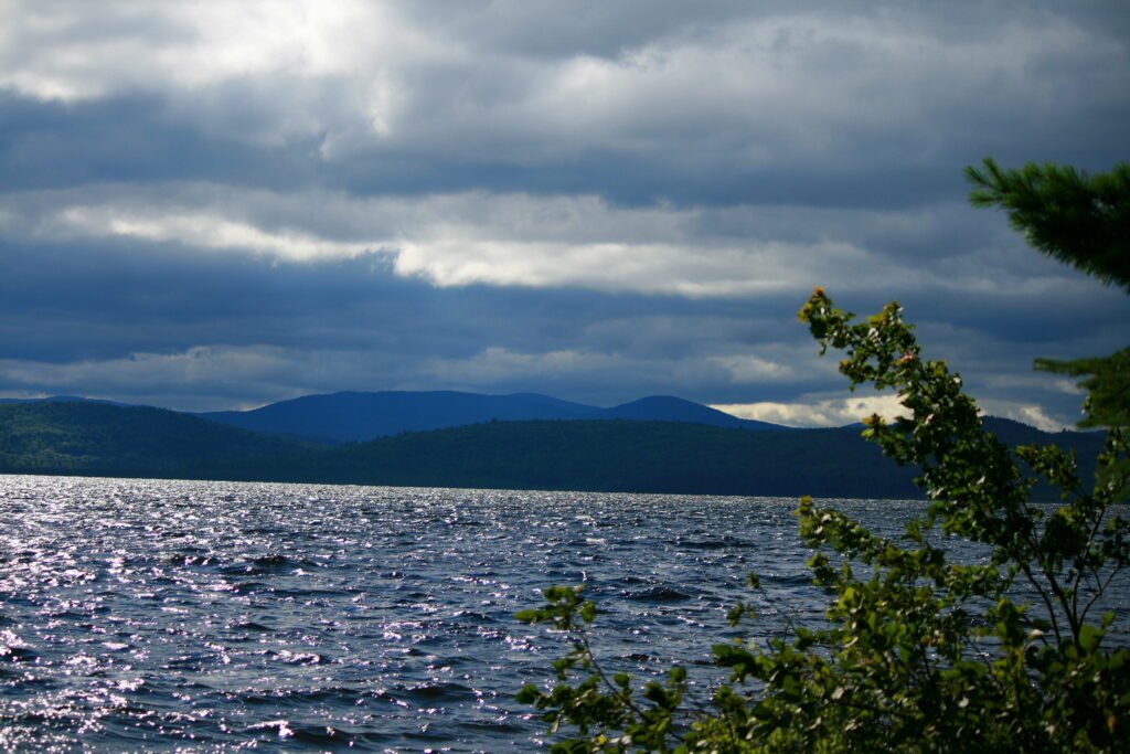 Distant dark mountains and choppy water under dramatic cloudy skies with sun reflecting on Lake Umbagog, New Hampshire