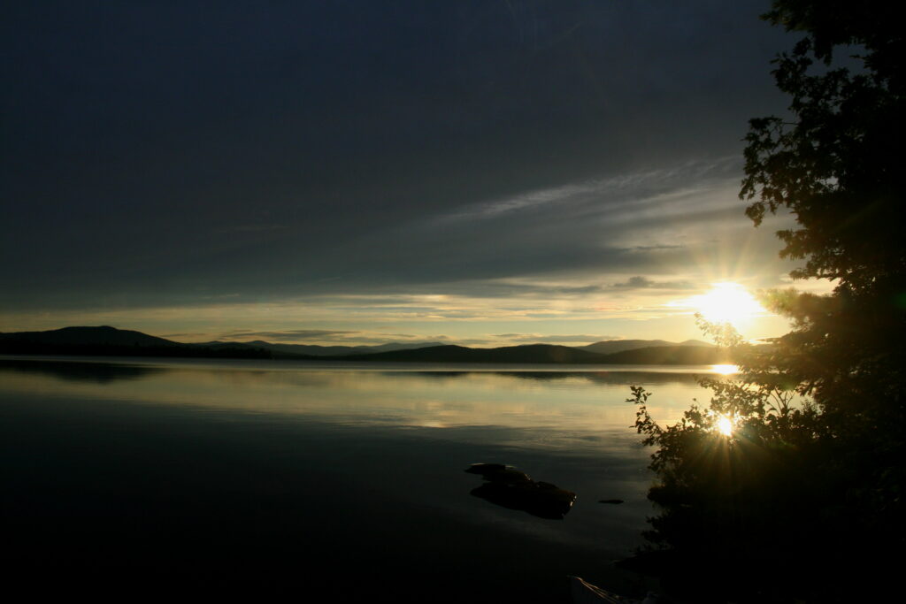 Golden sunset reflecting over the calm waters and silhouetted trees of Lake Umbagog