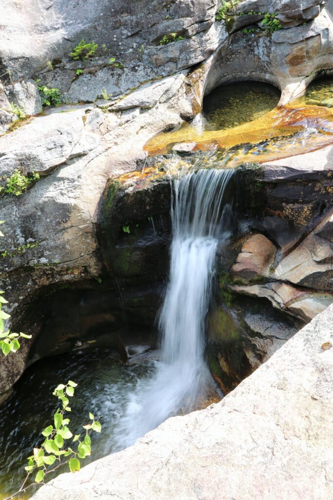 Water rushing and spilling over sculpted granite rock formations at Screw Auger Falls in Grafton Notch State Park, Maine.